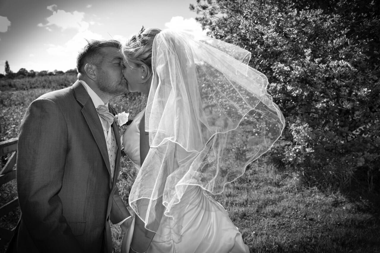 Wedding couple kiss as veil blows in wind