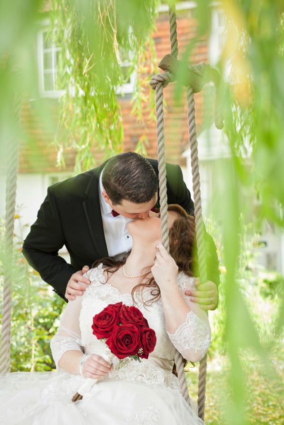Bride sat on swing being kissed