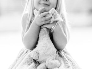 Little girl hugging soft toy, smiling with eyes closed.